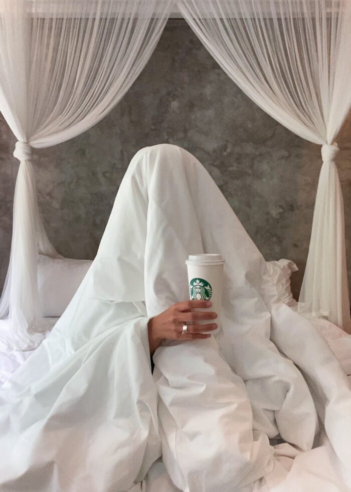 person hiding under the duvet and holding a starbucks drink